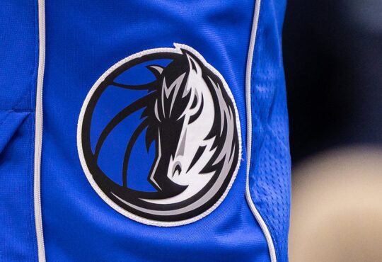 Close view of the Dallas Mavericks horse-head logo stitched on the leg of blue team shorts.