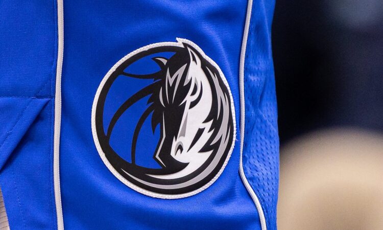 Close view of the Dallas Mavericks horse-head logo stitched on the leg of blue team shorts.