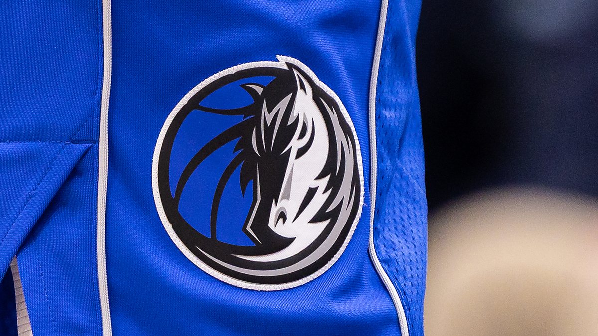 Close view of the Dallas Mavericks horse-head logo stitched on the leg of blue team shorts.