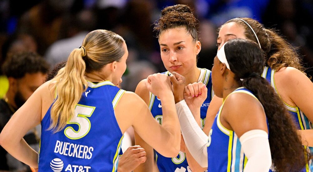 Dallas Wings guard Paige Bueckers huddles with teammates in blue uniforms at midcourt before tipoff.