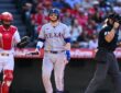 Texas Rangers catcher Danny Jansen walks away from the plate with his bat after striking out, the Angels catcher and umpire beside him.