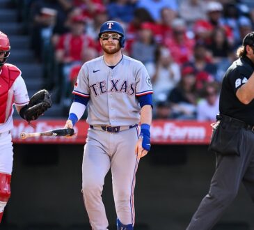 Texas Rangers catcher Danny Jansen walks away from the plate with his bat after striking out, the Angels catcher and umpire beside him.