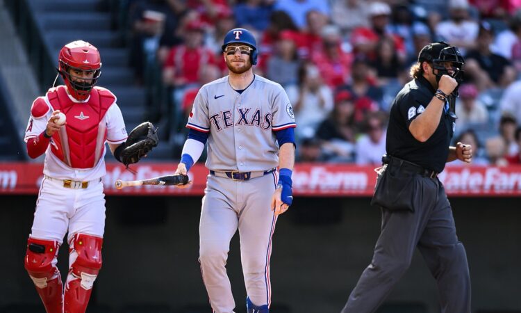 Texas Rangers catcher Danny Jansen walks away from the plate with his bat after striking out, the Angels catcher and umpire beside him.