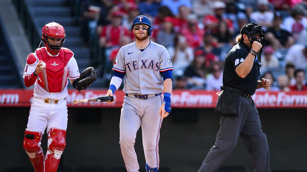 Texas Rangers catcher Danny Jansen walks away from the plate with his bat after striking out, the Angels catcher and umpire beside him.