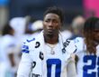 Dallas Cowboys linebacker DeMarvion Overshown stands on the sideline in uniform with a towel around his neck.