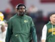 Green Bay Packers passing game coordinator Derrick Ansley watches from the sideline wearing a headset.