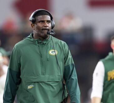 Green Bay Packers passing game coordinator Derrick Ansley watches from the sideline wearing a headset.