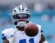 Dallas Cowboys defensive end Donovan Ezeiruaku reaches for a football during pregame warmups, the ball blurred in the foreground.