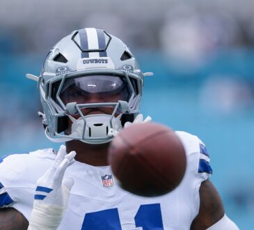 Dallas Cowboys defensive end Donovan Ezeiruaku reaches for a football during pregame warmups, the ball blurred in the foreground.