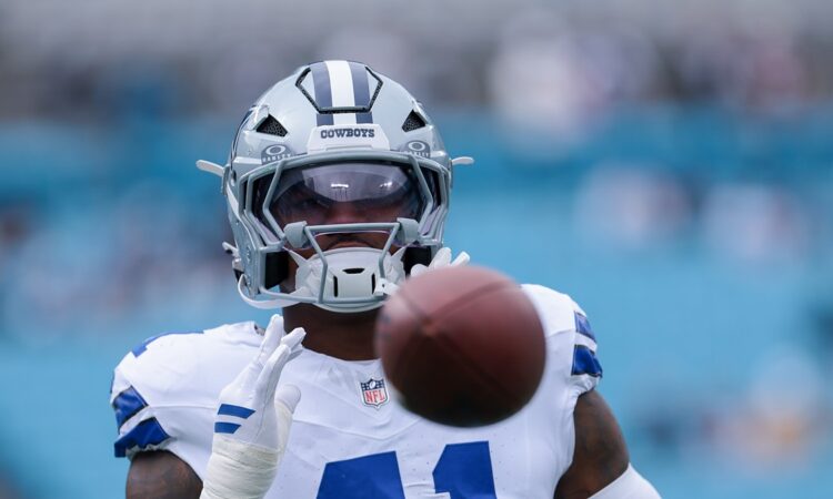 Dallas Cowboys defensive end Donovan Ezeiruaku reaches for a football during pregame warmups, the ball blurred in the foreground.