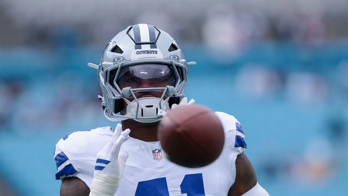 Dallas Cowboys defensive end Donovan Ezeiruaku reaches for a football during pregame warmups, the ball blurred in the foreground.