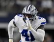 Dallas Cowboys defensive end Donovan Ezeiruaku fires off the line with his hand up in a white No. 41 jersey.