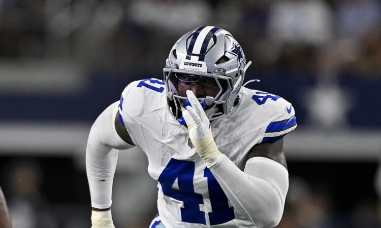 Dallas Cowboys defensive end Donovan Ezeiruaku fires off the line with his hand up in a white No. 41 jersey.