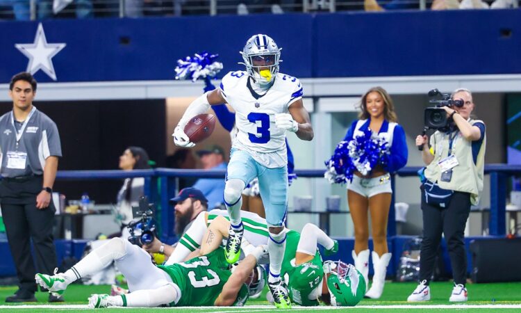 Dallas Cowboys wide receiver George Pickens carries the ball past two fallen Eagles defenders along the sideline.