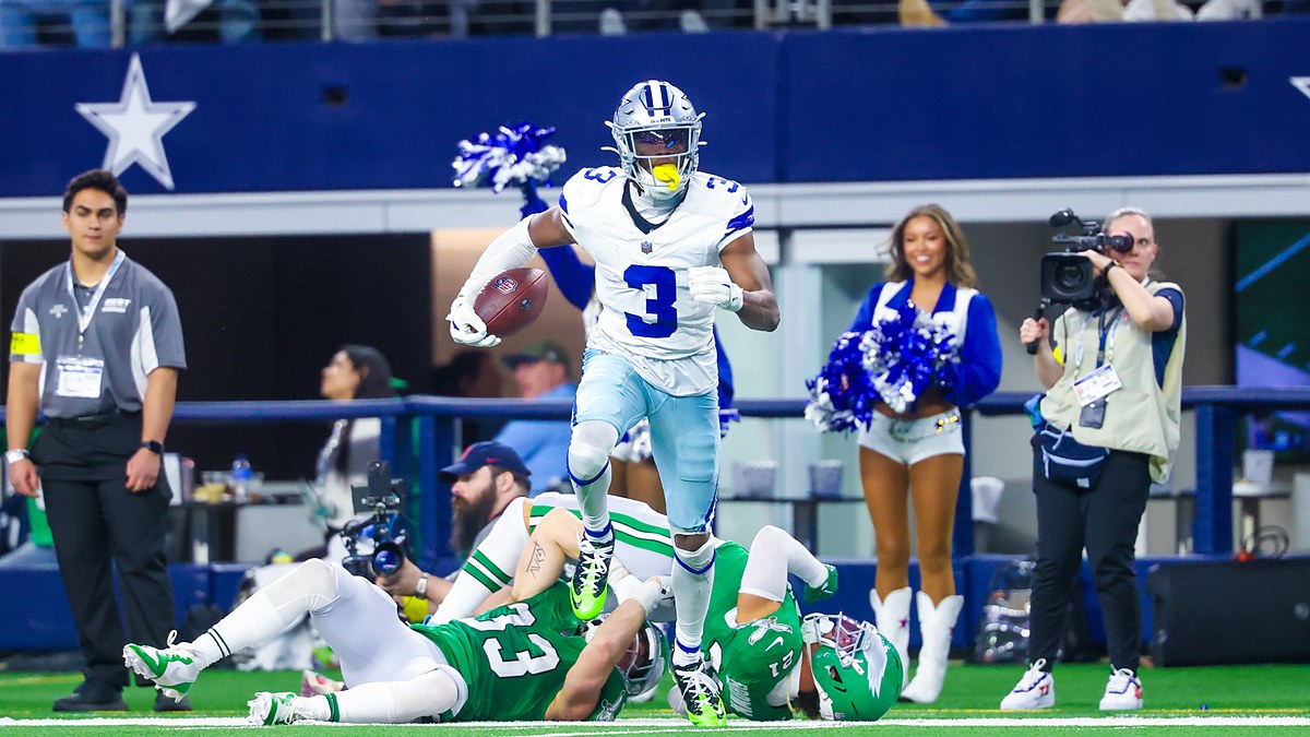 Dallas Cowboys wide receiver George Pickens carries the ball past two fallen Eagles defenders along the sideline.