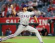 Texas Rangers pitcher Jacob deGrom strides toward the plate in road grays, ball hidden behind his hip.