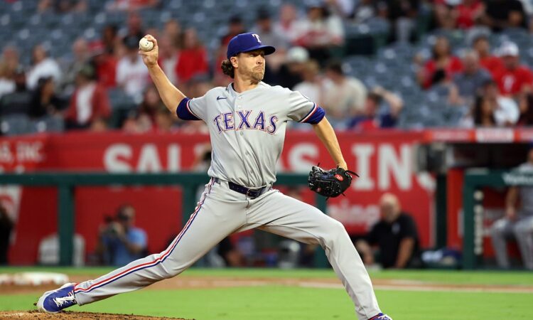 Texas Rangers pitcher Jacob deGrom strides toward the plate in road grays, ball hidden behind his hip.