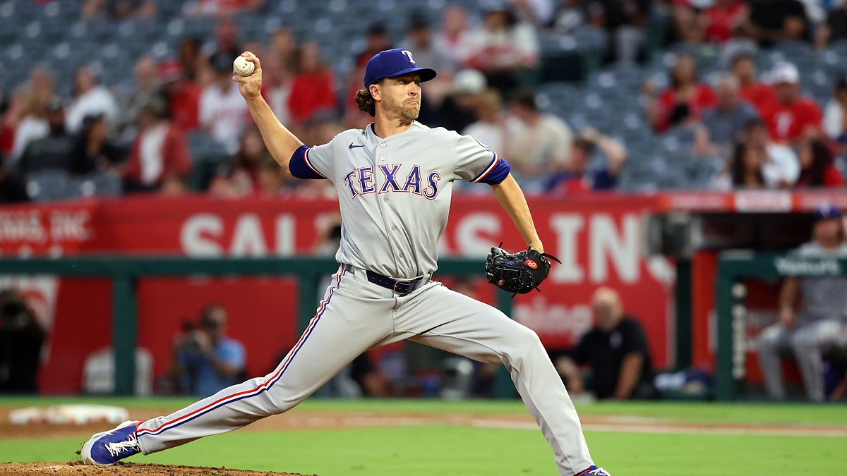 Texas Rangers pitcher Jacob deGrom strides toward the plate in road grays, ball hidden behind his hip.