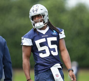 Dallas Cowboys linebacker Jaishawn Barham smiles toward a coach while standing on the practice field in helmet and jersey.