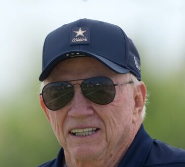Dallas Cowboys owner Jerry Jones smiles in a team cap and aviator sunglasses at training camp.