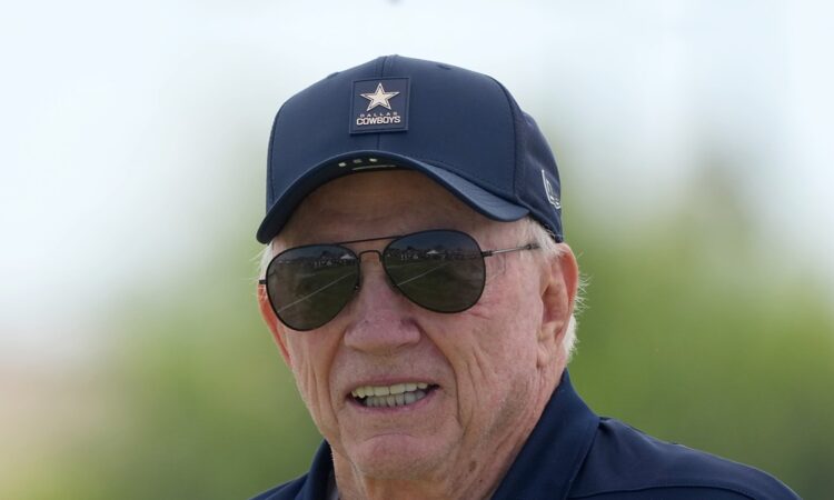 Dallas Cowboys owner Jerry Jones smiles in a team cap and aviator sunglasses at training camp.
