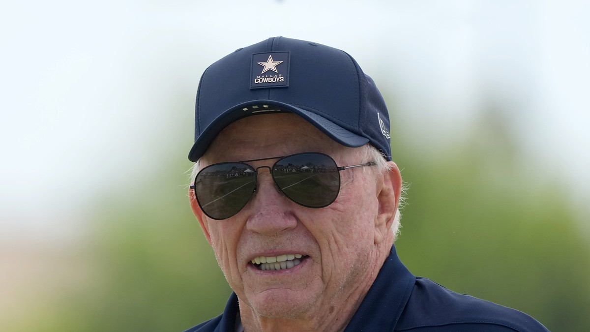Dallas Cowboys owner Jerry Jones smiles in a team cap and aviator sunglasses at training camp.