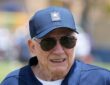 Dallas Cowboys owner Jerry Jones smiles on the practice field in a team cap and sunglasses at training camp.