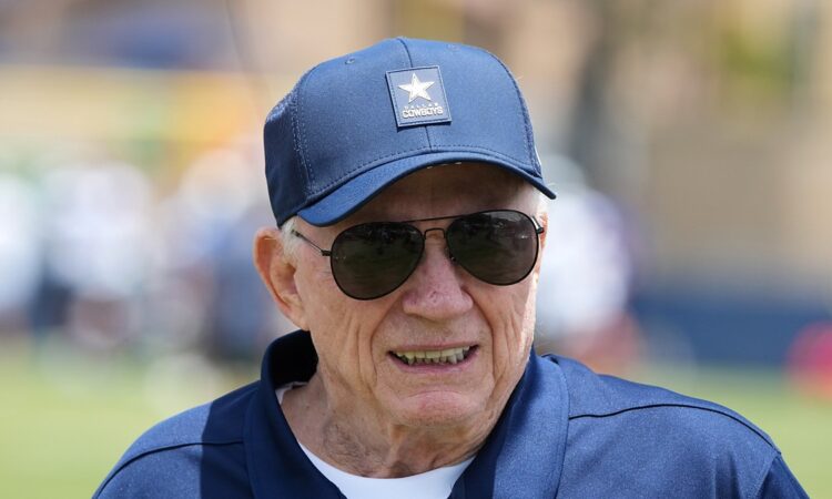 Dallas Cowboys owner Jerry Jones smiles on the practice field in a team cap and sunglasses at training camp.