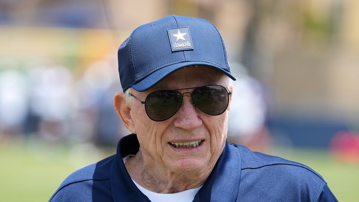 Dallas Cowboys owner Jerry Jones smiles on the practice field in a team cap and sunglasses at training camp.