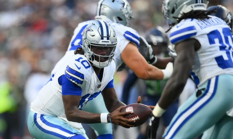 Dallas Cowboys quarterback Joe Milton III extends the ball on a handoff to a teammate in the backfield.