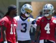 Dallas Cowboys wide receiver George Pickens smiles with an arm around quarterback Dak Prescott as Joe Milton III looks on.