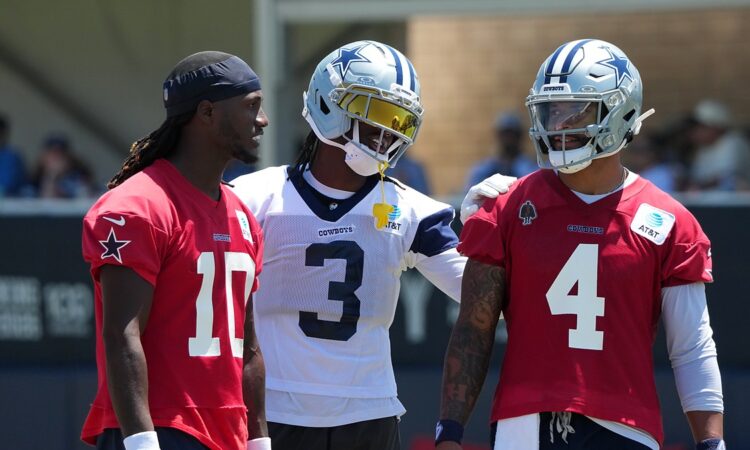 Dallas Cowboys wide receiver George Pickens smiles with an arm around quarterback Dak Prescott as Joe Milton III looks on.
