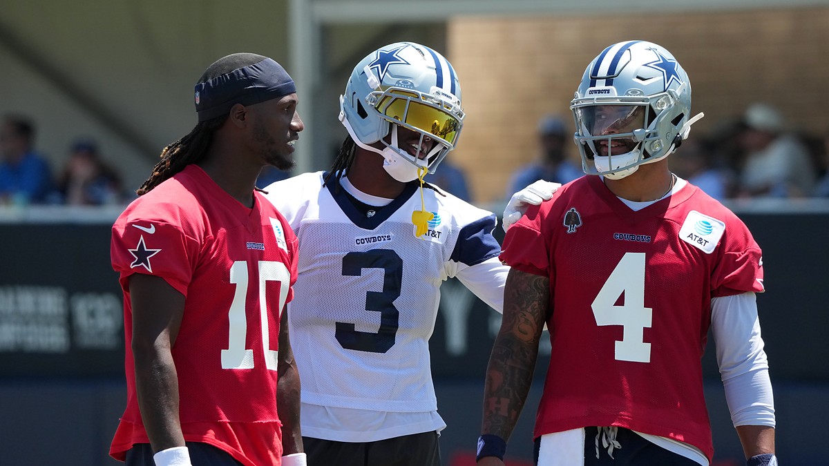 Dallas Cowboys wide receiver George Pickens smiles with an arm around quarterback Dak Prescott as Joe Milton III looks on.