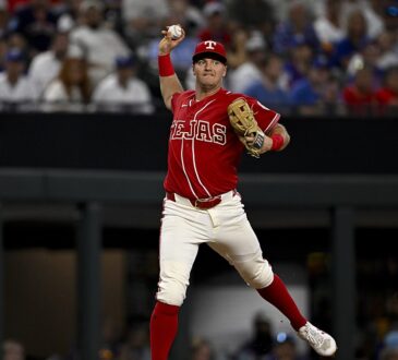 Texas Rangers third baseman Josh Jung cocks his arm to throw across the diamond in a red Tejas City Connect uniform.