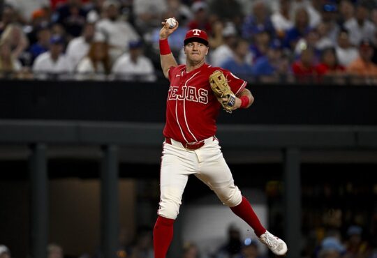 Texas Rangers third baseman Josh Jung cocks his arm to throw across the diamond in a red Tejas City Connect uniform.