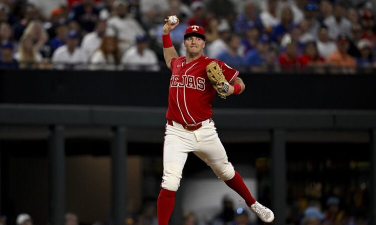 Texas Rangers third baseman Josh Jung cocks his arm to throw across the diamond in a red Tejas City Connect uniform.