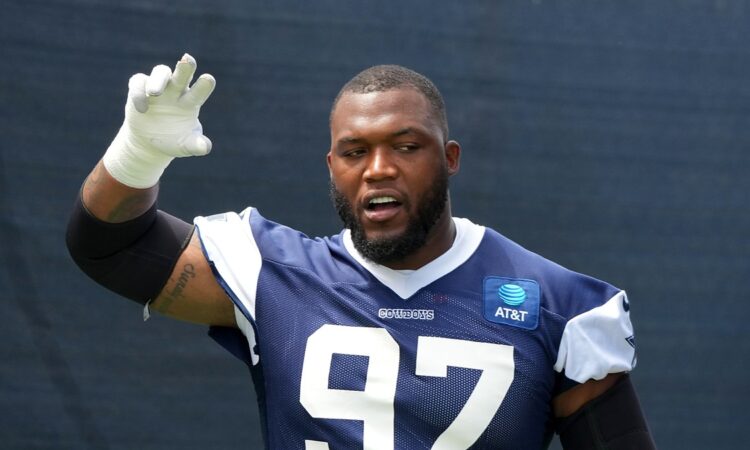 Dallas Cowboys defensive tackle Kenny Clark raises a taped hand while talking during training camp in a navy No. 97 jersey.