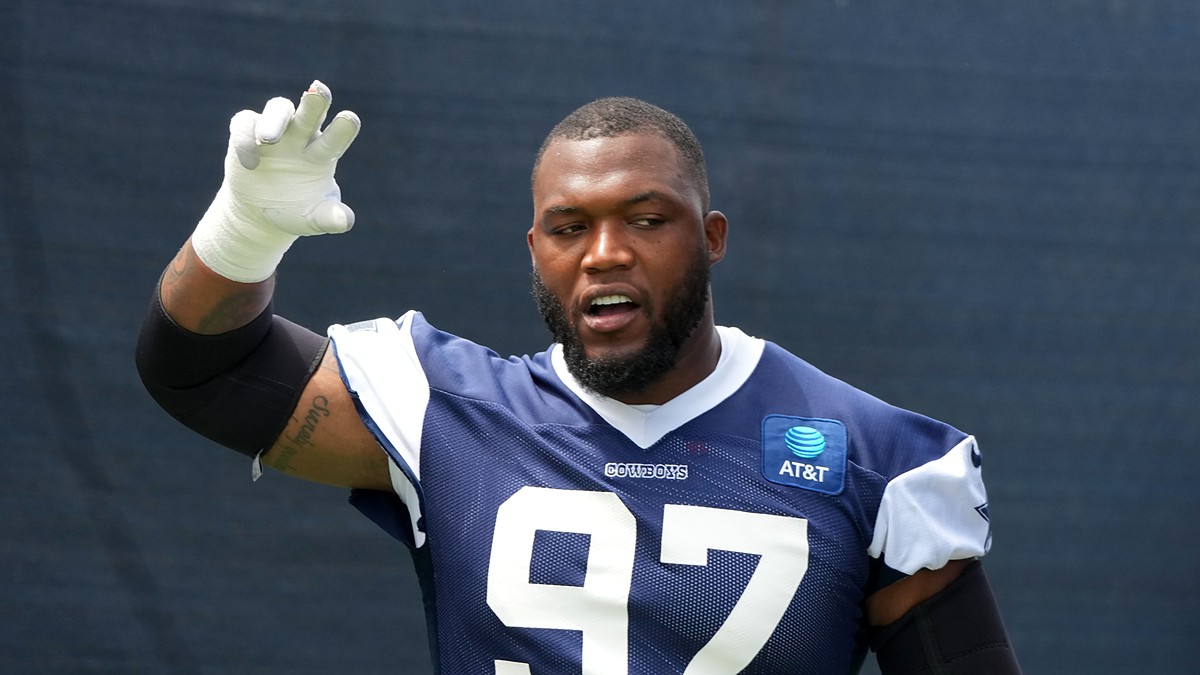Dallas Cowboys defensive tackle Kenny Clark raises a taped hand while talking during training camp in a navy No. 97 jersey.