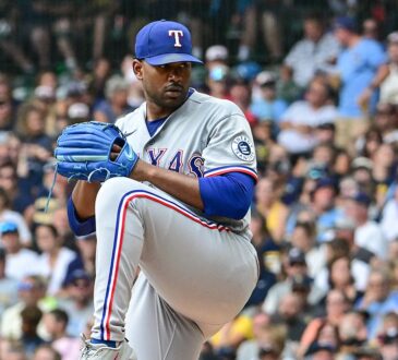 Texas Rangers pitcher Kumar Rocker lifts his front leg in his windup in a gray road uniform at American Family Field.