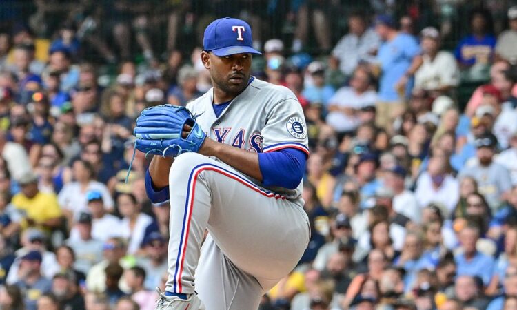 Texas Rangers pitcher Kumar Rocker lifts his front leg in his windup in a gray road uniform at American Family Field.