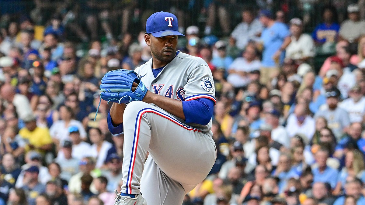 Texas Rangers pitcher Kumar Rocker lifts his front leg in his windup in a gray road uniform at American Family Field.