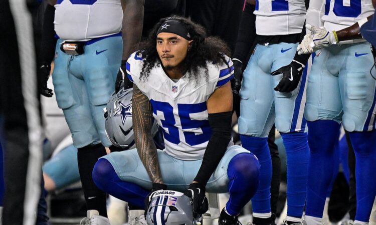 Dallas Cowboys linebacker Marist Liufau crouches on the sideline with his helmet on the turf in front of him.