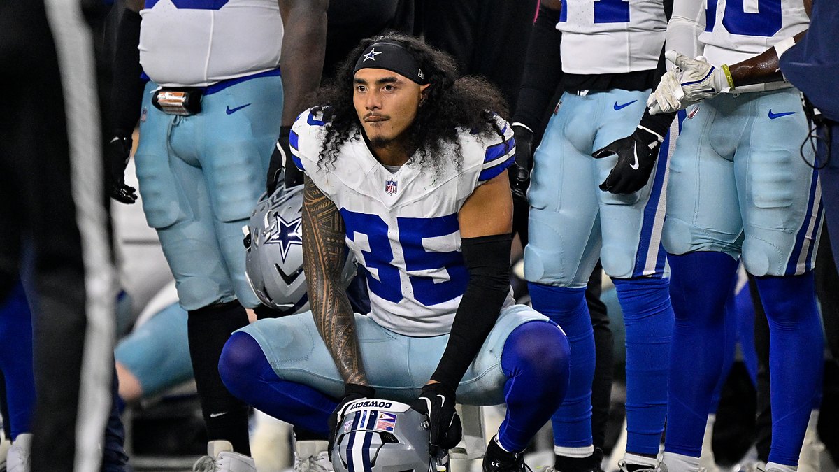 Dallas Cowboys linebacker Marist Liufau crouches on the sideline with his helmet on the turf in front of him.