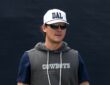 Dallas Cowboys special teams coordinator Nick Sorensen watches practice in a white DAL cap and sunglasses.