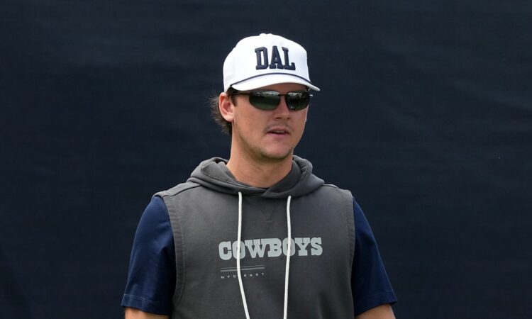 Dallas Cowboys special teams coordinator Nick Sorensen watches practice in a white DAL cap and sunglasses.