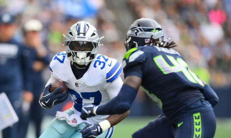 Dallas Cowboys running back Phil Mafah tucks the ball and cuts upfield as a Seattle Seahawks defender closes in.
