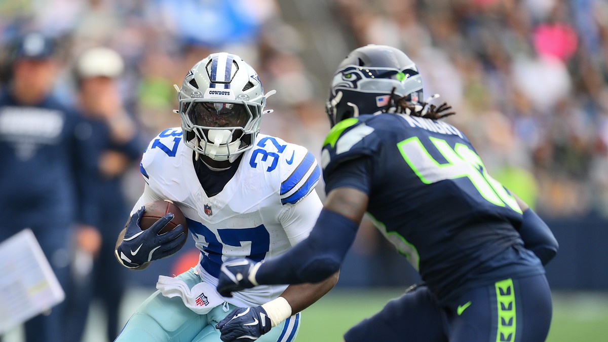 Dallas Cowboys running back Phil Mafah tucks the ball and cuts upfield as a Seattle Seahawks defender closes in.