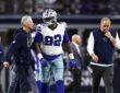 Dallas Cowboys defensive tackle Quinnen Williams walks off the field flanked by two team trainers.