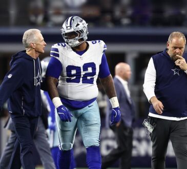 Dallas Cowboys defensive tackle Quinnen Williams walks off the field flanked by two team trainers.