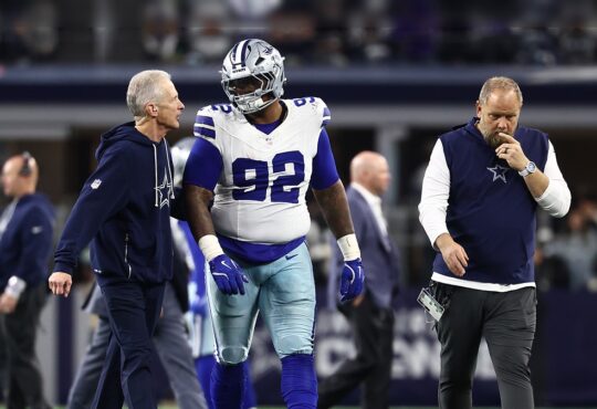 Dallas Cowboys defensive tackle Quinnen Williams walks off the field flanked by two team trainers.